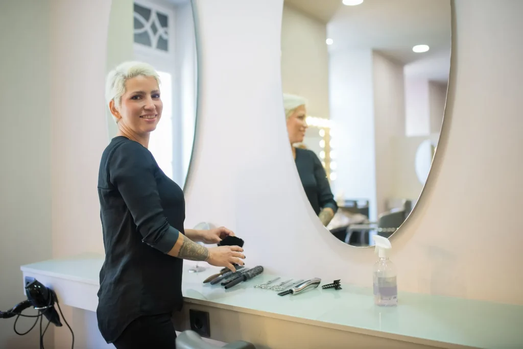 Cabeleireira de cabelo branco curto a preparar ferramentas junto a espelhos redondos