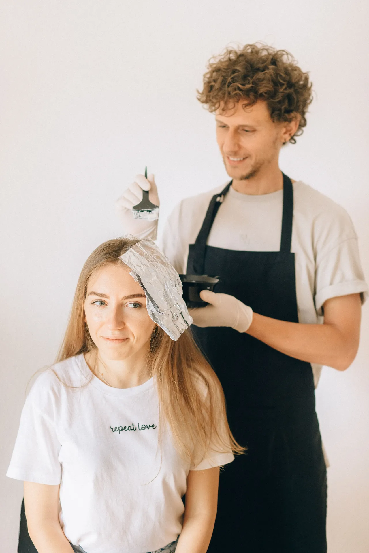 Cabeleireiro a aplicar coloração no cabelo de uma cliente sentada no salão