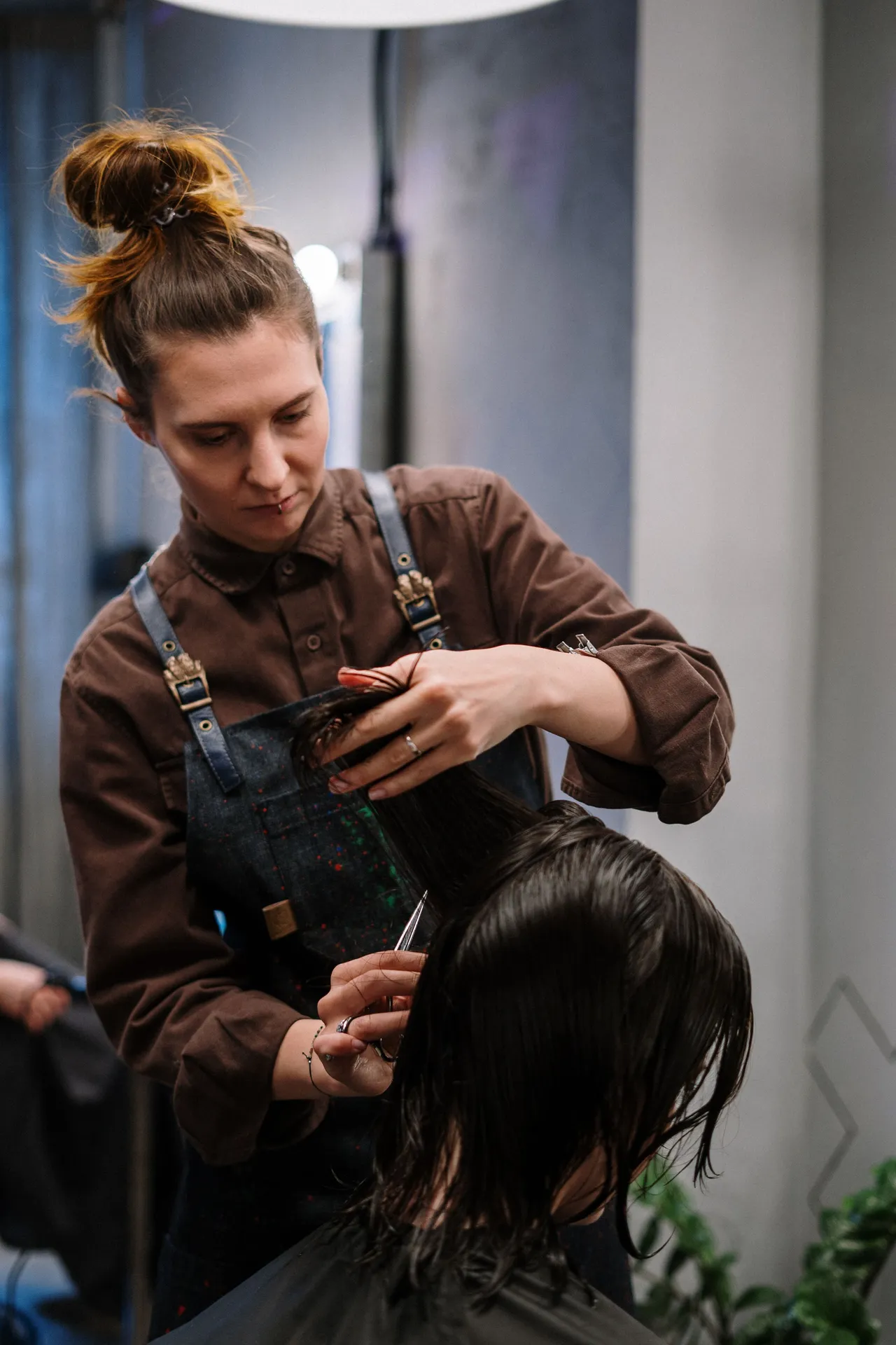 Cabeleireira a cortar o cabelo de uma cliente num salão com plantas