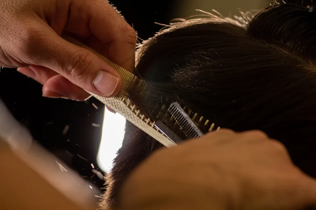 Mãos de cabeleireira a cortar uma madeixa de cabelo com pente e tesoura